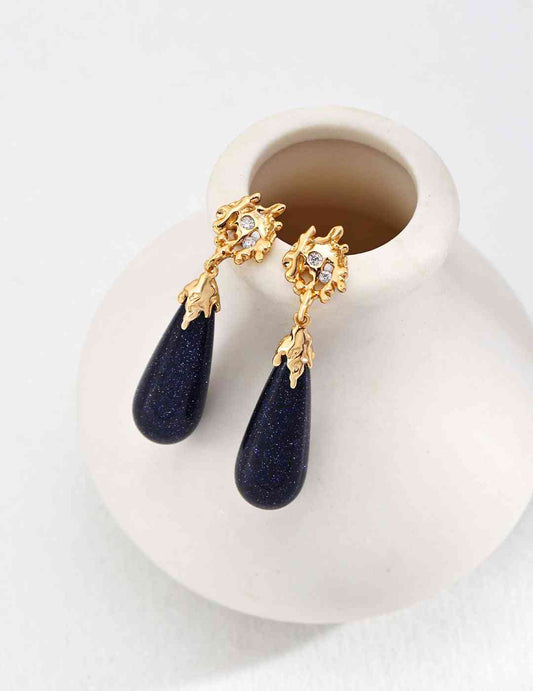 a white vase with a pair of blue sandstone and gold earrings