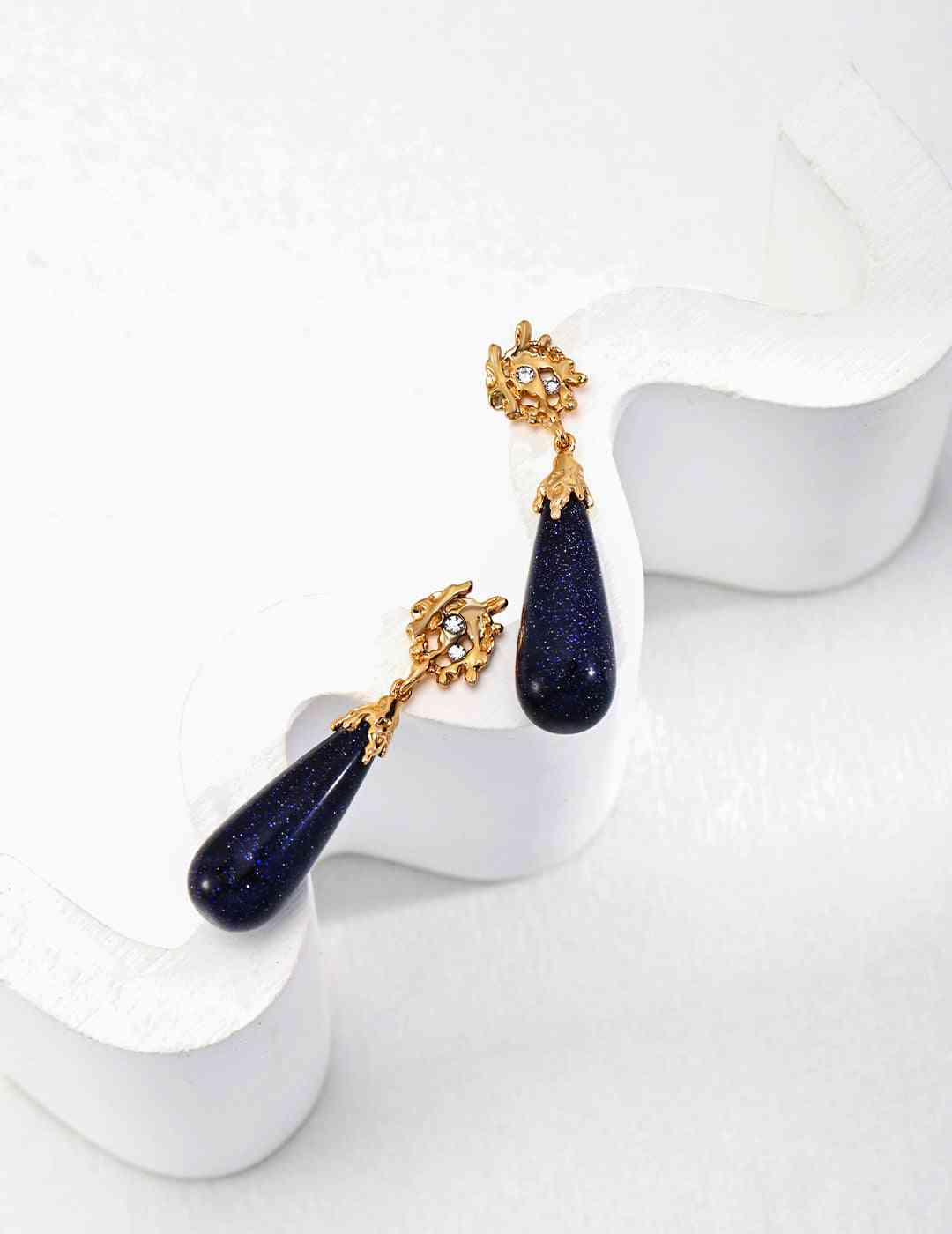 a pair of blue sandstone and gold earrings on a white surface