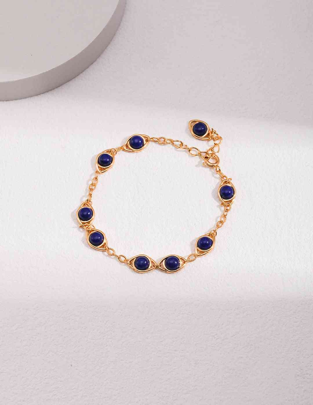 a gold bracelet with blue beads on a white surface