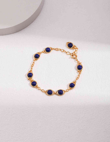 a gold bracelet with blue beads on a white surface