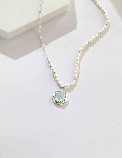 a white peal and silver necklace with a blue stone on it