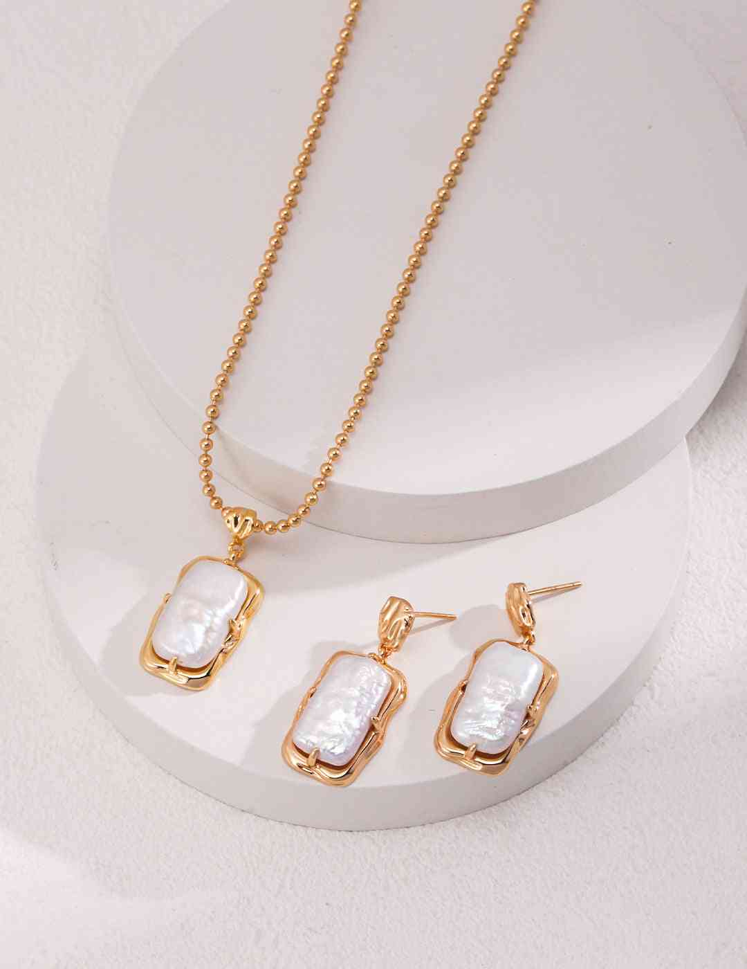 Gold pearl necklace and earrings set on circular display