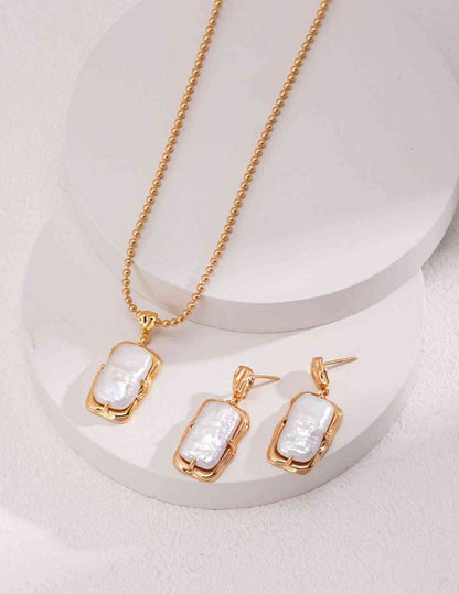 Gold pearl necklace and earrings set on circular display