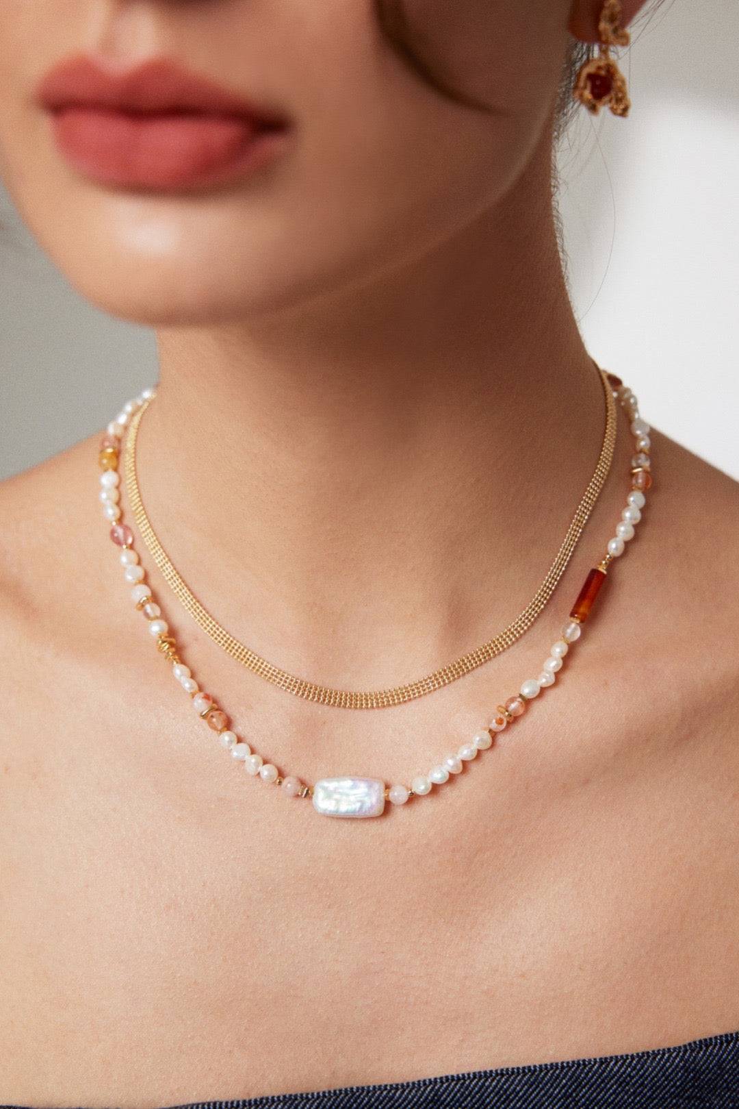 a close up of a woman wearing a strawberry quartz and pearl necklace