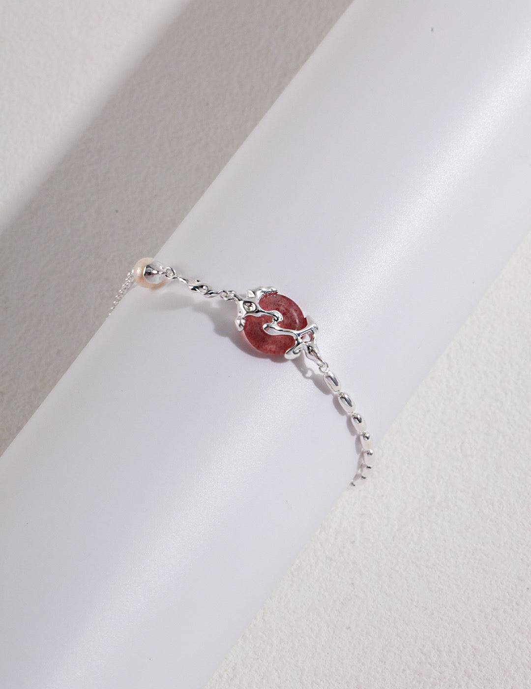 a close up of a piece of strawberry quartz and silver bracelet on a white surface