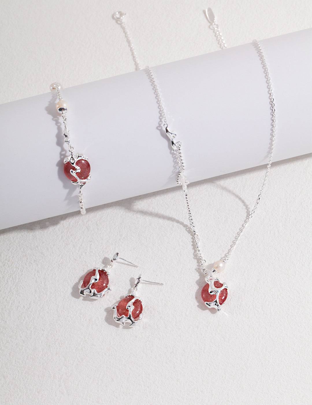 a strawberry quartz and silver necklace, earrings, and ring are on a white surface