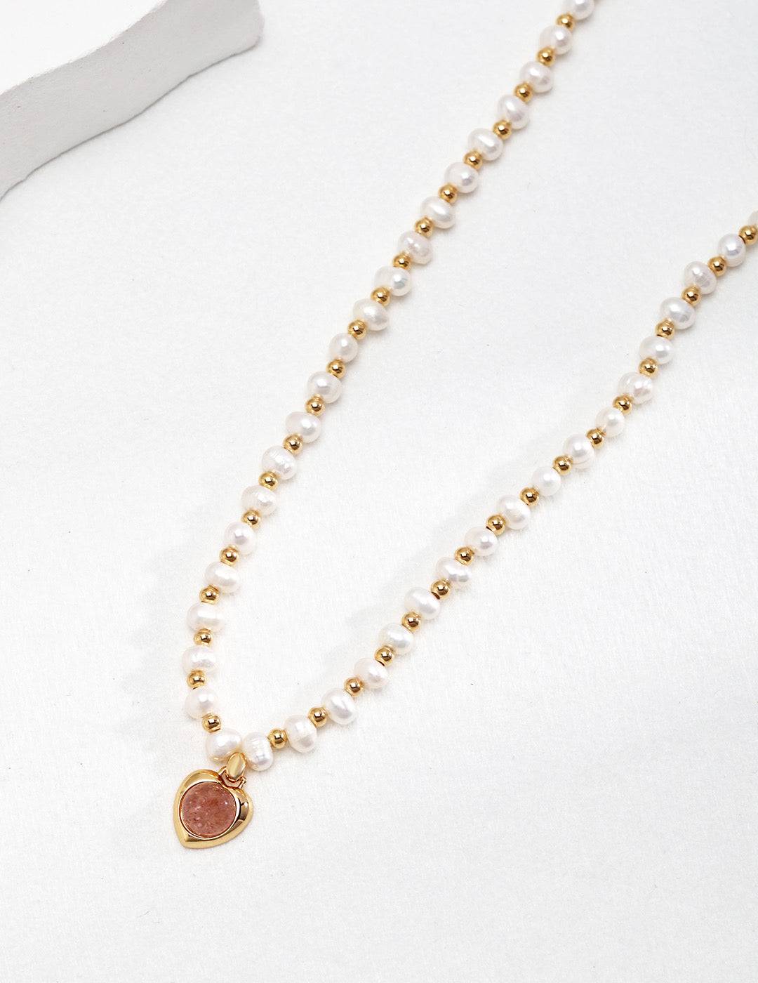 a pearl necklace with a gold strawberry quartz heart charm