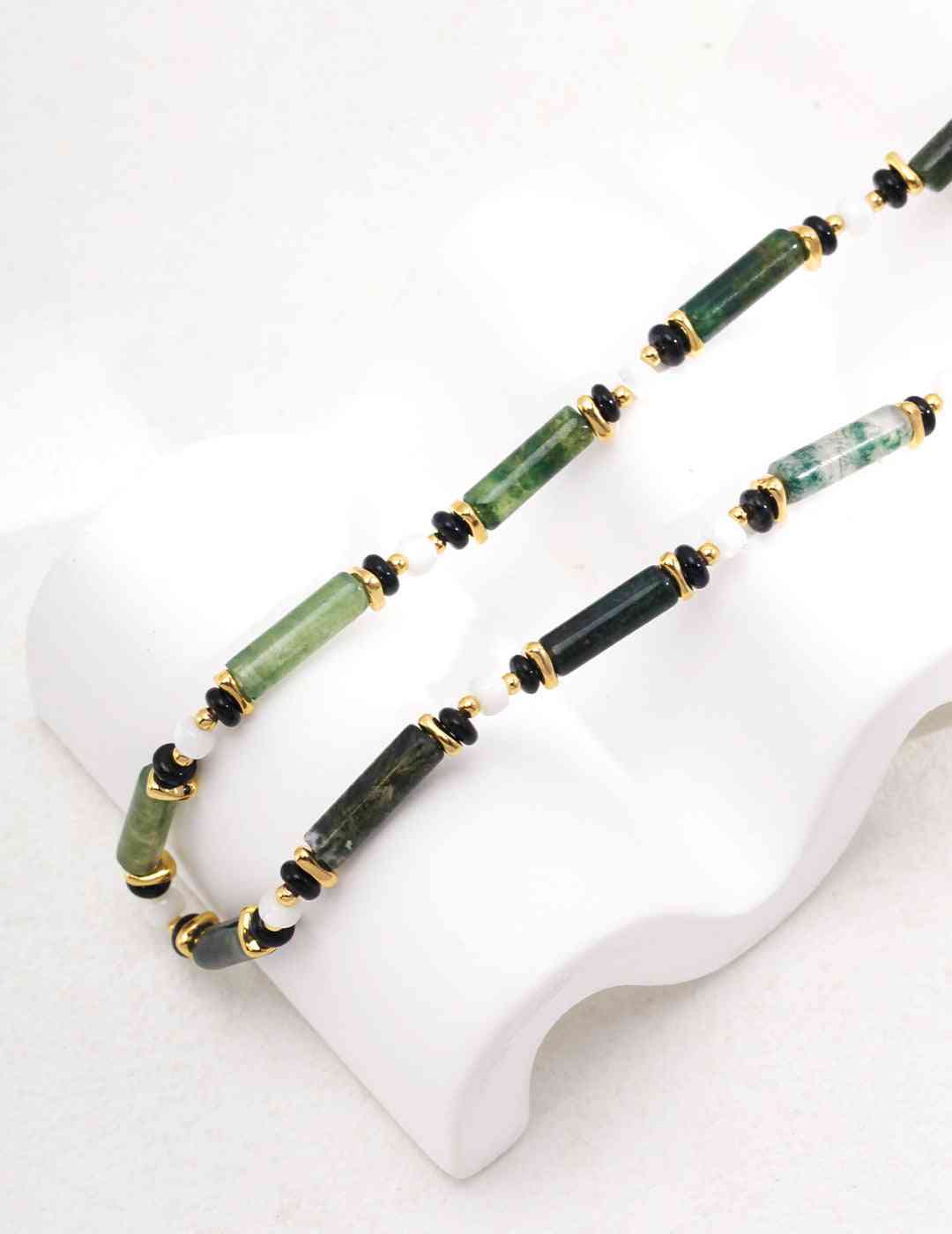 a green and black agate beaded necklace on a white stand