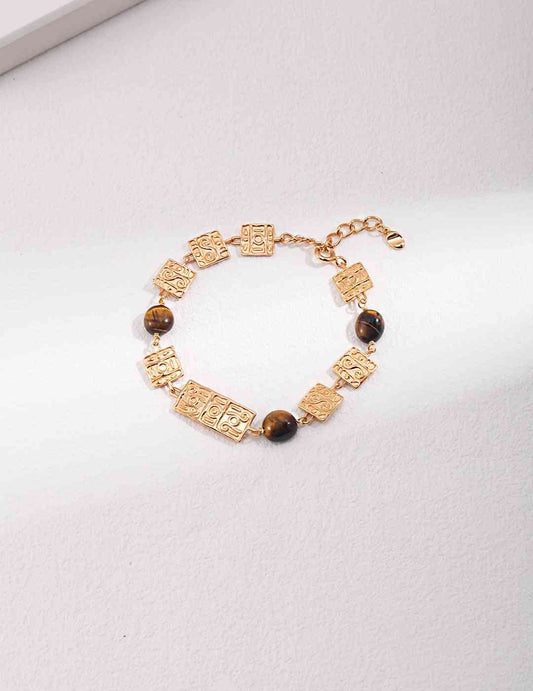 a gold bracelet with brown tiger's eye beads and a cross