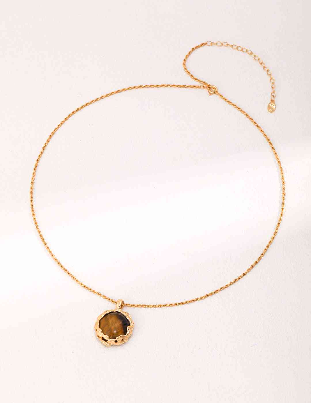 a gold necklace with a brown tiger's eye stone on a white background