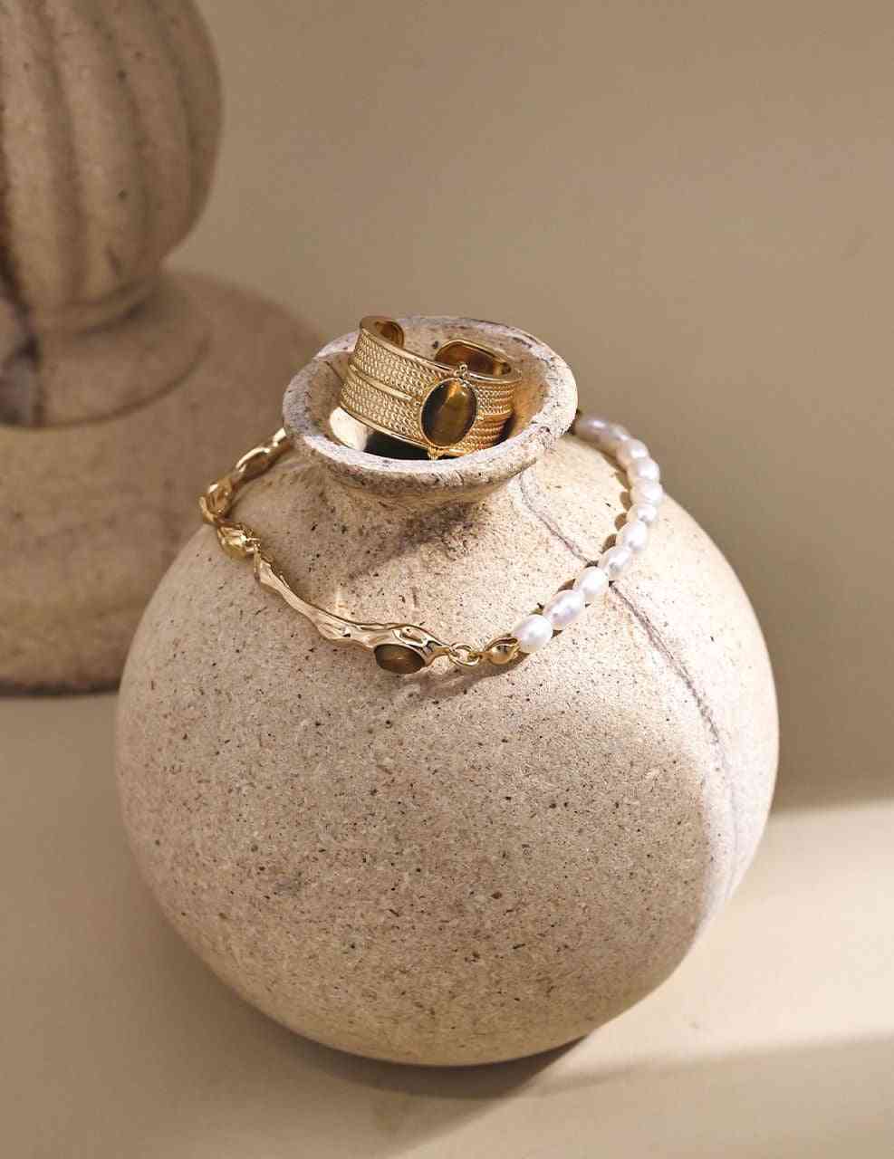 a white vase with a gold ring and bracelet on it